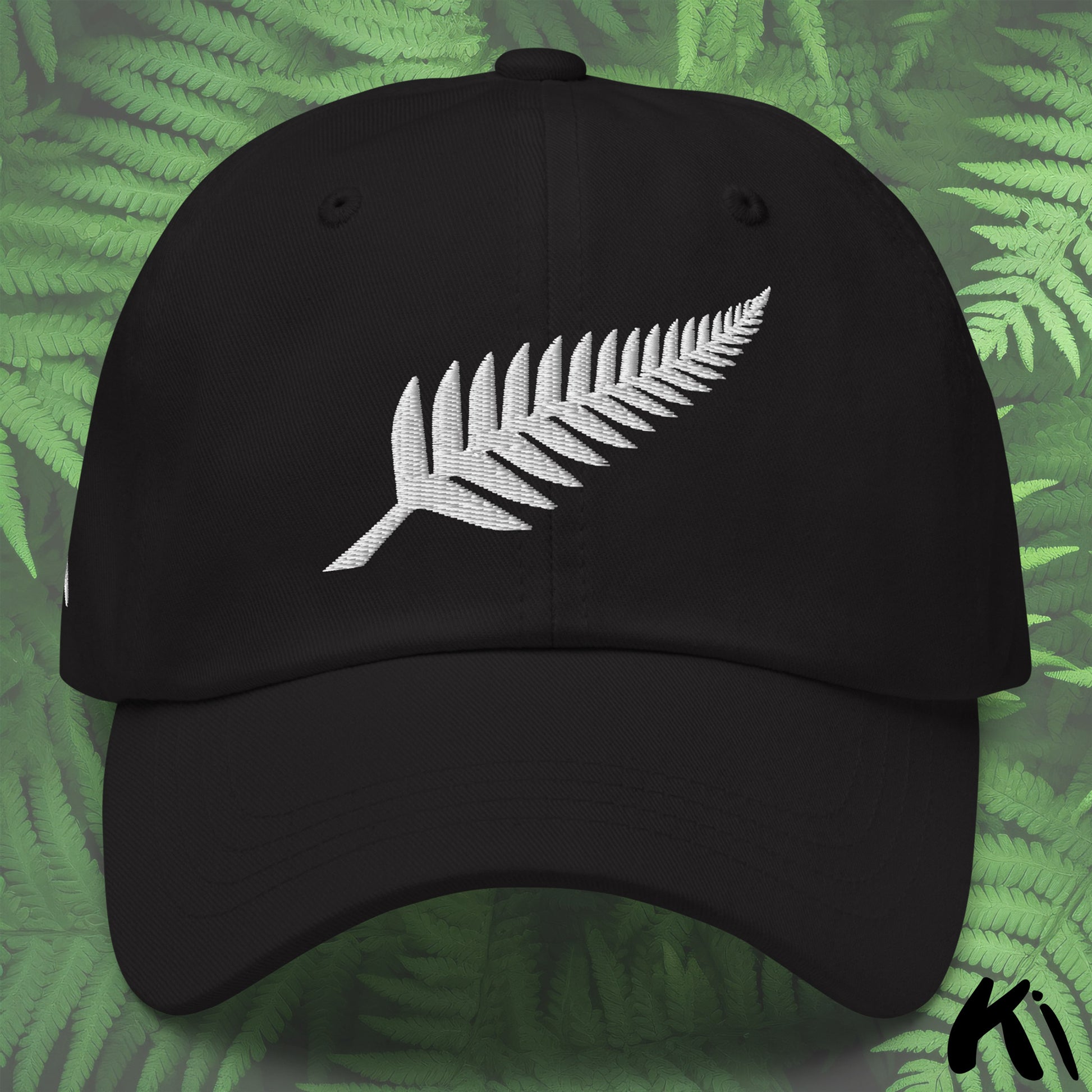 Black cap with white fern leaf design on a green leafy background